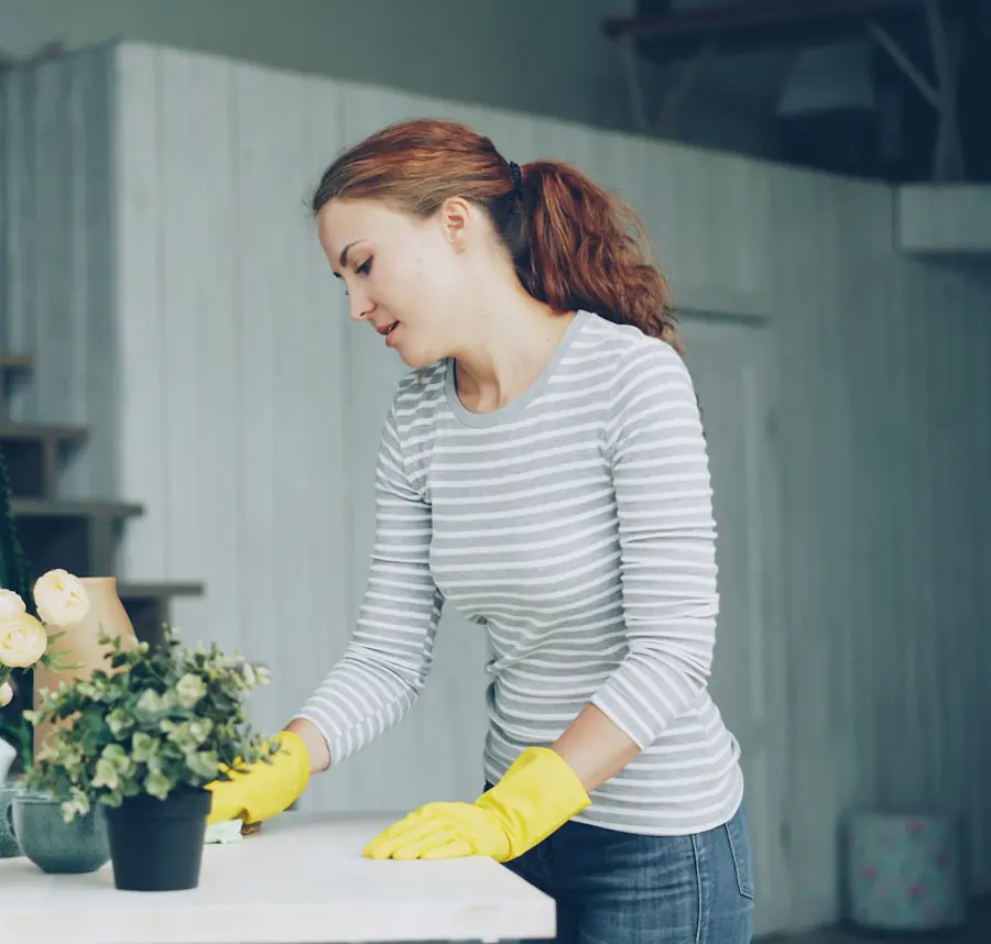 A cleaner in yellow gloves wiping a table beside fresh flowers