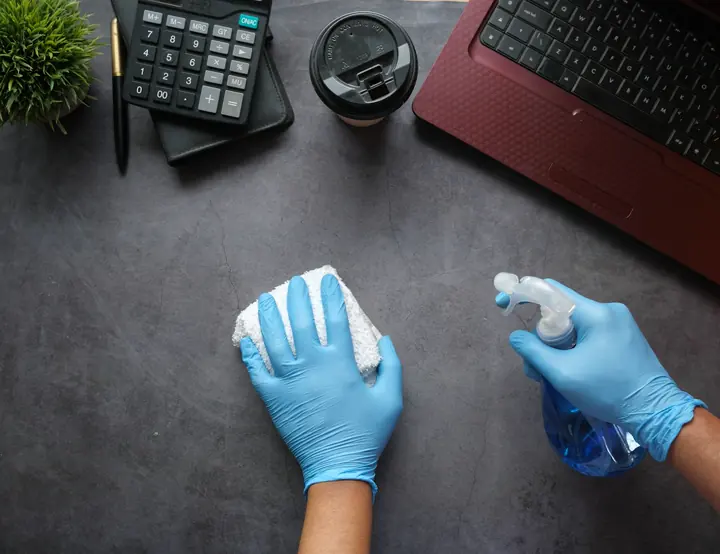 Gloved hands disinfecting an office desk
