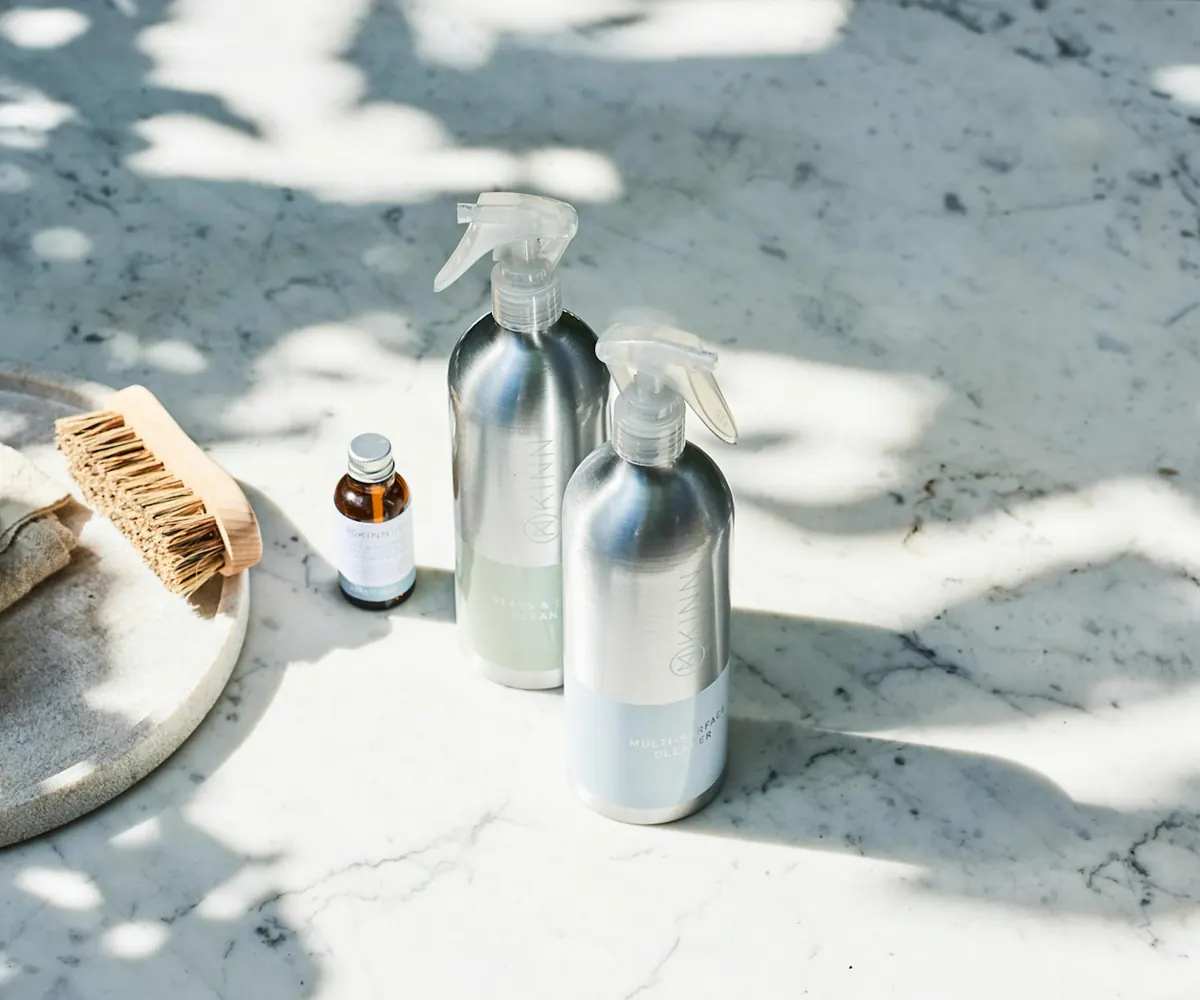 Natural cleaning supplies: refillable spray bottles and a wooden brush on a marble counter